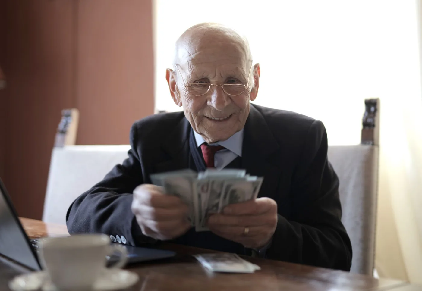 Usměvavý senior počítá bankovky u stolu