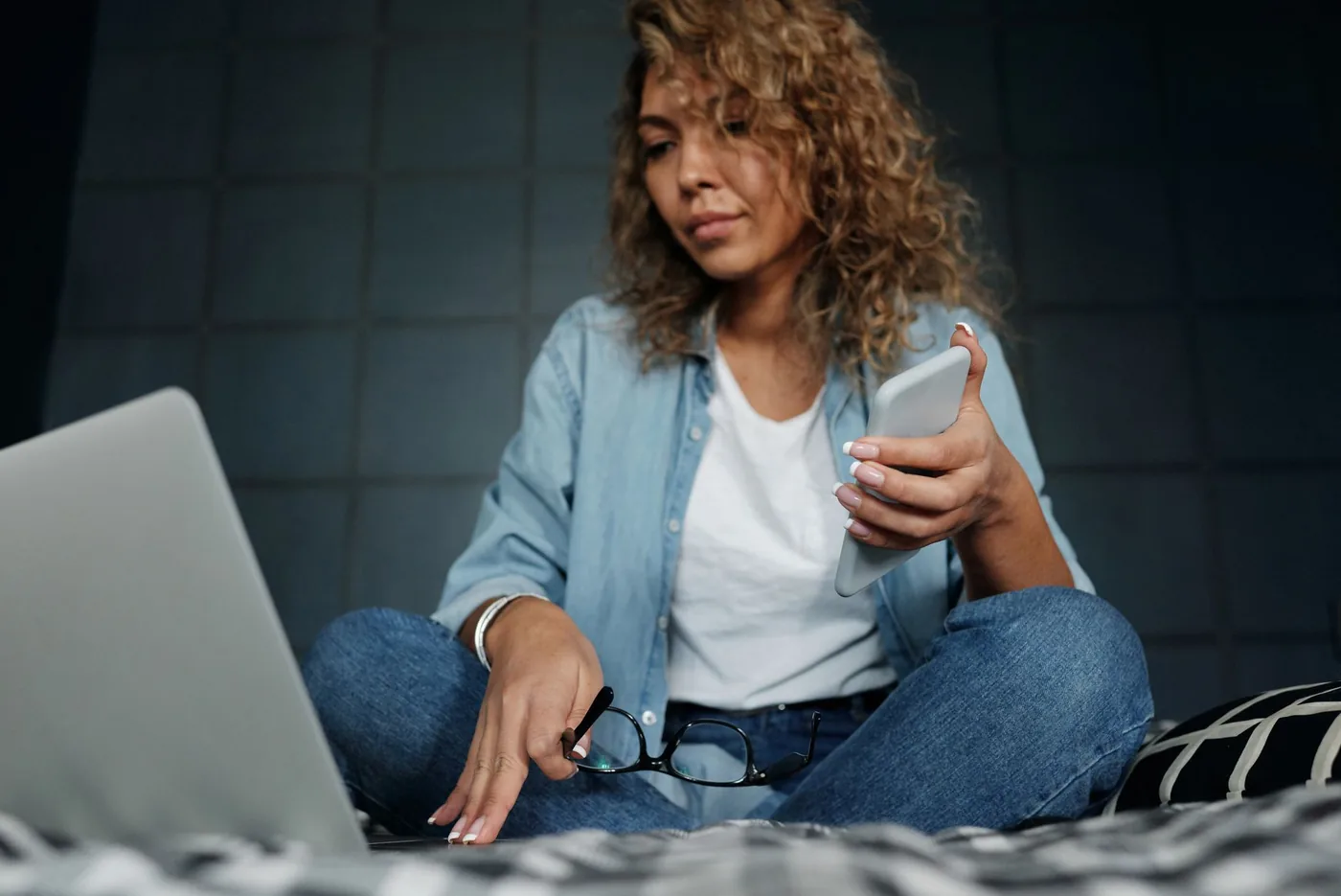 Žena na posteli porovnává nabídky na laptopu a mobilu